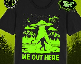 May include: A black t-shirt with a green glow-in-the-dark design featuring a UFO, Bigfoot, and a creature with wings. The text "WE OUT HERE" is written below the design. The text "SPECIAL GLOW OPTION ON T-SHIRTS ONLY" is in the top right corner. The text "AVAILABLE ON: T-SHIRTS - TANKS - LONG SLEEVES - SWEATSHIRTS - HOODIES" is at the bottom of the image.
