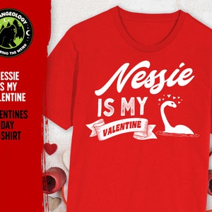 May include: Red t-shirt with a white graphic that says "Nessie is my Valentine" with a cartoon image of the Loch Ness Monster and hearts.