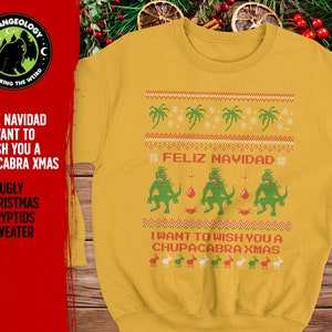 May include: A yellow Christmas sweater with a festive design featuring a green monster, palm trees, and the text "Feliz Navidad" and "I want to wish you a Chupacabra Xmas".