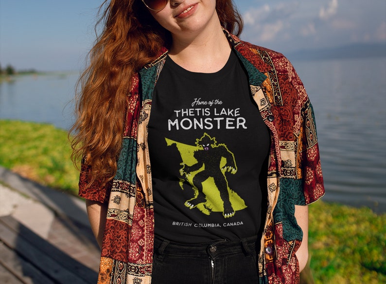 K&ouml;nnte beinhalten: Schwarzes T-Shirt mit einer gr&uuml;nen Silhouette eines Monsters und dem Text "Home of the Thetis Lake Monster" und "British Columbia, Canada".