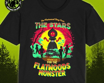 May include: Black t-shirt with a graphic of a red-headed, black-robed figure with glowing red eyes and outstretched arms. The text "The Mechanical Thing From THE STARS" is above the figure, and "Watch out FOR THE FLATWOODS MONSTER" is below the figure.