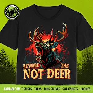 Pu&ograve; includere: Una maglietta nera con una grafica di un cervo con occhi rossi che ringhia e ha grandi corna. Il cervo &egrave; su uno sfondo di fiamme e una foresta. Il testo "Beware the Not Deer" &egrave; stampato sotto il cervo.