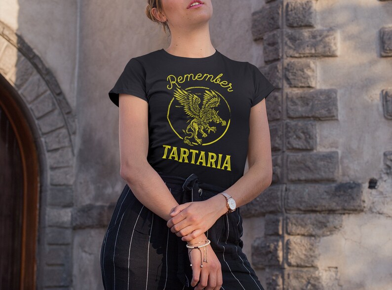 Peut inclure: Un t-shirt noir avec un motif jaune d'un griffon avec le texte "Remember Tartaria" imprim&eacute; dessus.