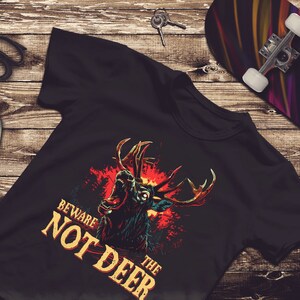 Pu&ograve; includere: Maglietta nera con una grafica di un cervo ruggente con fiamme rosse e gialle dietro. Il testo "Beware the Not Deer" &egrave; stampato in giallo sulla maglietta.