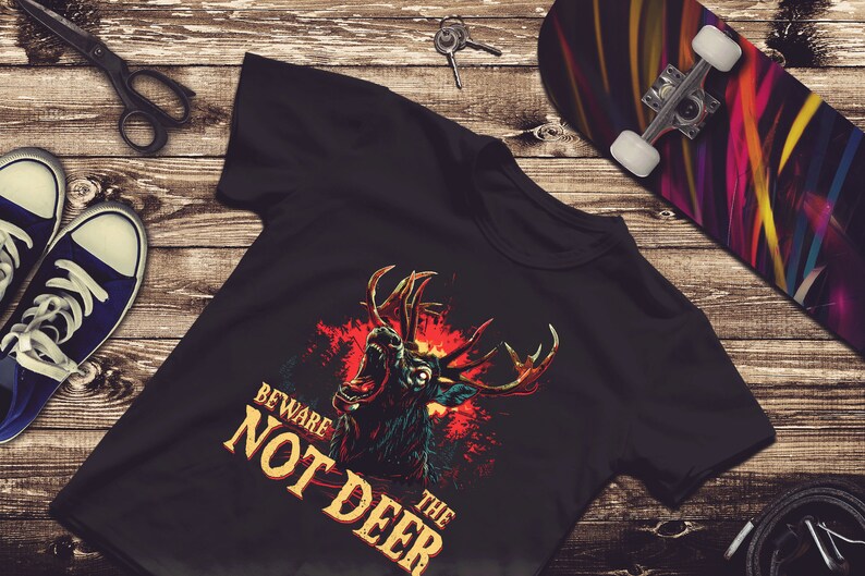Pu&ograve; includere: Maglietta nera con una grafica di un cervo ruggente con fiamme rosse e gialle dietro. Il testo "Beware the Not Deer" &egrave; stampato in giallo sulla maglietta.