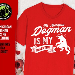 May include: Red t-shirt with a white graphic that says "The Michigan Dogman is my Valentine" with a drawing of a dogman and hearts.