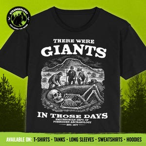 May include: Black t-shirt with a white graphic design featuring a skeleton digging up a giant bone. The text reads "There Were Giants In Those Days" and "Smithsonian Dept. of Forbidden Archaeology Est. 1877".