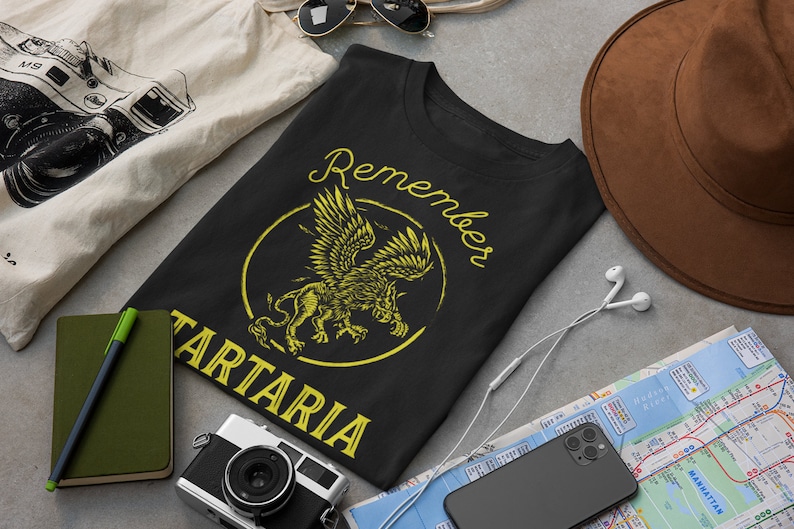 Peut inclure: T-shirt noir avec un graphique jaune d'un lion ail&eacute; avec le texte "Remember Tartaria" dans un cercle.