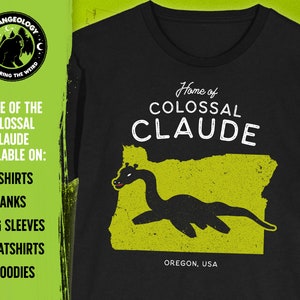 May include: Black t-shirt with a green graphic of the state of Oregon and a black silhouette of a sea monster. The text "Home of Colossal Claude" is printed in white on the shirt. The text "Oregon, USA" is printed in white at the bottom of the graphic.