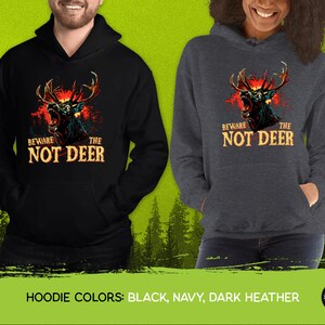 Pu&ograve; includere: Felpe con cappuccio nere, blu navy e grigio scuro con una grafica di un cervo con occhi rossi luminosi e il testo "Beware the Not Deer".