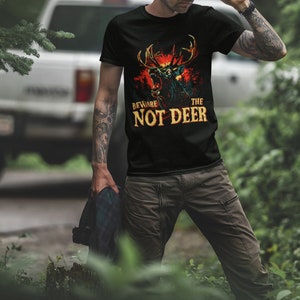 Pu&ograve; includere: Una maglietta nera con una grafica di un cervo con occhi rossi luminosi e il testo "Beware the Not Deer".