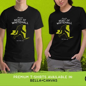 May include: Two black t-shirts with a yellow graphic of a Bigfoot-like creature walking across a silhouette of New York State. The text "Home of the Beast of Whitehall" is printed above the graphic. The text "New York, USA" is printed below the graphic.