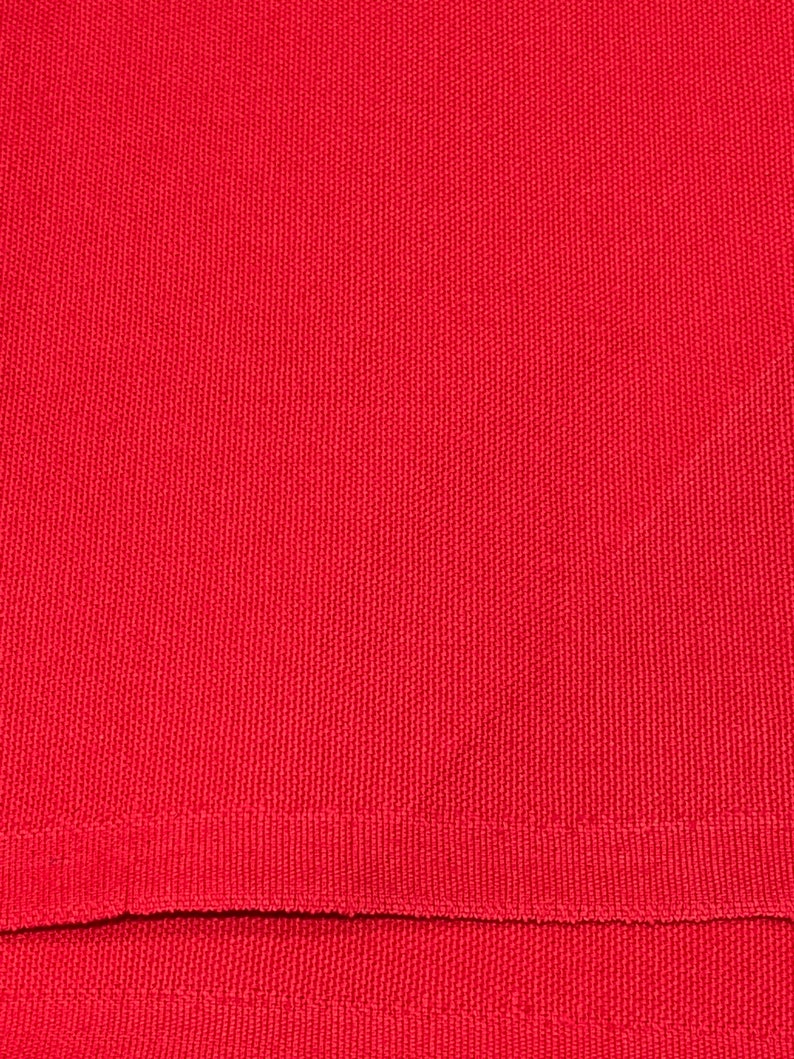 May include: Close-up of a solid red fabric with a textured weave. The fabric has a ribbed hem at the bottom. The color is a vibrant, saturated red.