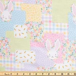 May include: A patchwork fabric design featuring pastel squares with floral, polka dot, and gingham patterns. Bunny faces and carrot motifs are interspersed throughout the design. The fabric is measured with an inch ruler.