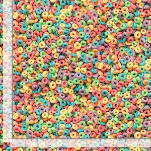 May include: A close-up shot of colorful, ring-shaped cereal pieces. The cereal pieces are in various colors, including red, yellow, green, purple, and orange. A ruler is visible along the left side of the image, with measurements in inches.