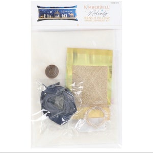 May include: A craft kit for decorating a bench pillow with a Nativity scene. The kit includes a blue and gold pillow, gold glitter, blue ribbon, and gold wire.