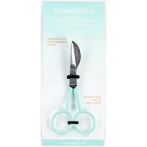May include: Mint green Kimberbell Duckbill Applique Scissors. The scissors have a curved blade and double-loop rings. The packaging includes text that reads "Smoothly clip small applique pieces" and "Double-loop rings fit every hand."