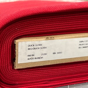 May include: A roll of red duck cloth fabric. The label reads "DUCK CLOTH RED DUCK CLOTH" and "060 IN". The fabric is 100% cotton and professional cleaning is recommended. Made in India.