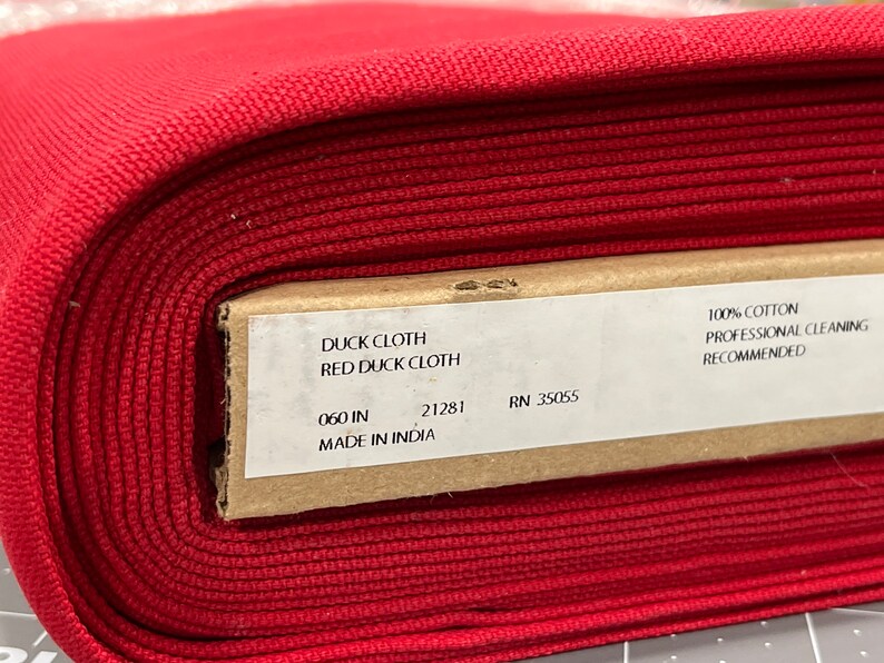 May include: A roll of red duck cloth fabric. The label reads "DUCK CLOTH RED DUCK CLOTH" and "060 IN". The fabric is 100% cotton and professional cleaning is recommended. Made in India.