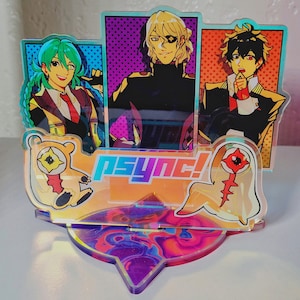 Könnte beinhalten: Ein bunter Acryl-Ständer mit drei Anime-Charakteren, einem Geist und einem Bären. Der Ständer hat eine holografische Oberfläche und der Text "psyNc!" ist auf der Vorderseite aufgedruckt.