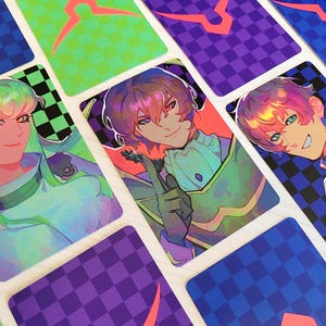 May include: A collection of anime-style character art cards. Each card features a different character with vibrant hair and clothing. The cards have a checkered pattern on the back, with a geometric design. The color palette includes green, purple, blue, and red.