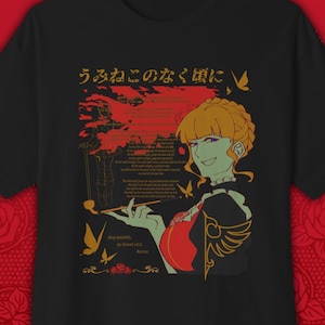 Può includere: Una t-shirt nera con una stampa grafica di un personaggio dai capelli biondi che tiene in mano una pipa. Il design include testo giapponese in alto, testo inglese al centro e farfalle gialle. Il personaggio indossa un abito scuro con dettagli rossi.