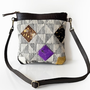 Könnte beinhalten: Eine kleine, schwarze und weiße Patchwork-Umhängetasche mit einem braunen Lederriemen. Die Tasche hat einen Reißverschluss und ist mit bunten Lederflicken verziert.