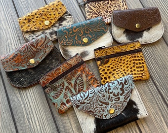 May include: Assortment of eight small leather coin purses with various embossed patterns and colours. The purses are made of cowhide and have a zipper closure.