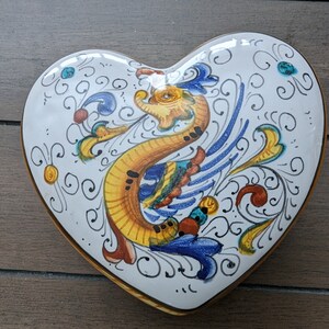 May include: White heart-shaped ceramic dish with a hand-painted design of a yellow, blue and green bird with intricate floral details.