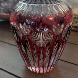 Könnte beinhalten: Eine rubinrote Glasvase mit aufwendigen Schliffmustern. Die Vase hat eine breite Öffnung und einen schmalen Boden.
