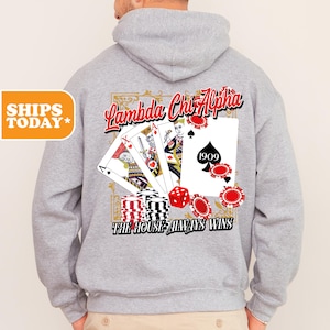 May include: A light gray hooded sweatshirt featuring a back graphic of playing cards, red and black poker chips, and a red die. The text reads Lambda Chi Alpha and The House Always Wins, with the year 1909 printed on the ace of spades card.