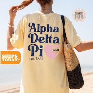 May include: A yellow t-shirt with a blue and white graphic that says "Alpha Delta Pi est. 1851" with a pink heart that has the letters "AΔΠ" inside.