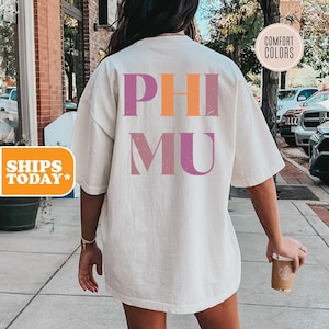 May include: White t-shirt with the letters "PHI MU" printed on the back in pink, orange, and purple. The letters have a distressed, vintage look.