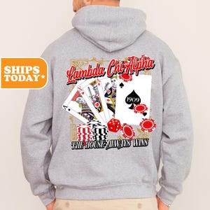 May include: A gray hooded sweatshirt with a design featuring playing cards, dice, and the text "Lambda Chi Alpha" and "The House Always Wins".