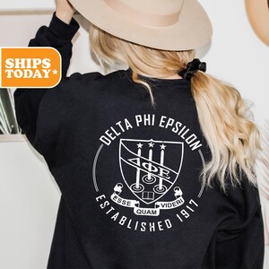 May include: Black sweatshirt with a white graphic of a shield with the text "Delta Phi Epsilon Established 1917" and the letters "DPE" inside the shield.