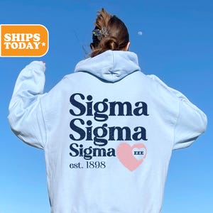 May include: Light blue hoodie with a black graphic that says "Sigma Sigma Sigma est. 1898" and a pink heart with the letters "EEE" inside.
