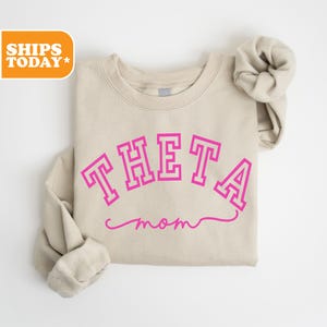 May include: A beige sweatshirt with the text "THETA mom" in pink lettering.