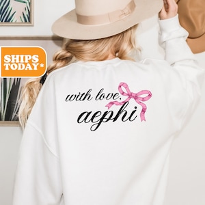 May include: White sweatshirt with the text "with love, aephi" and a pink bow.