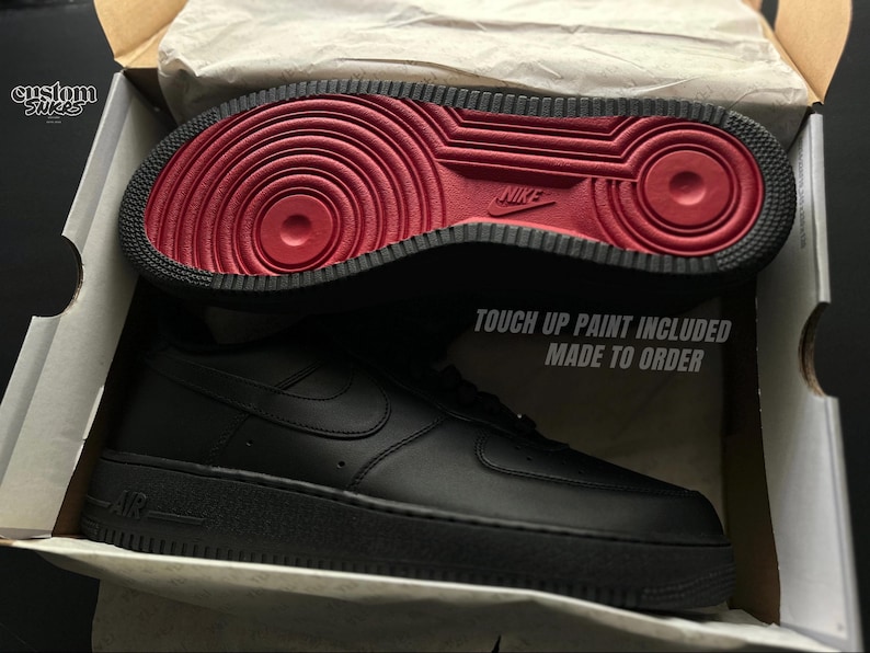 May include: Black leather sneaker with a red sole, displayed in an open box. The sole features a circular pattern and the Nike logo. The text "TOUCH UP PAINT INCLUDED MADE TO ORDER" is visible on the box.