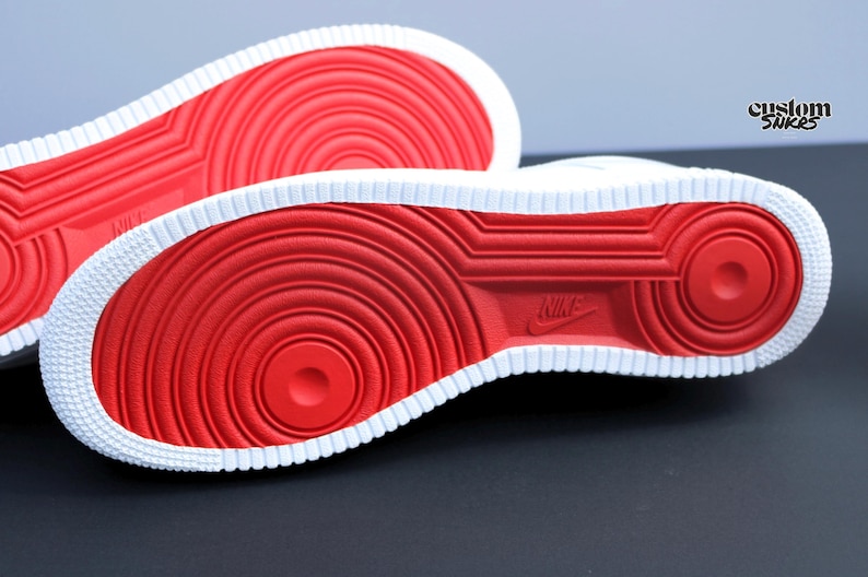 May include: Close-up of the soles of two white sneakers with red circular patterns and a white border. The Nike logo is visible on the sole. The sneakers are on a dark surface.