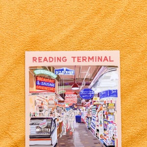 May include: A colourful illustration of the Reading Terminal Market in Philadelphia, Pennsylvania. The illustration shows a bustling market with vendors selling food and other goods. The text "Reading Terminal Market" is at the top of the illustration, and the text "Market" is at the bottom.