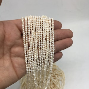 May include: A strand of white freshwater pearls, approximately 2-3 mm in size, strung on a thin thread. The pearls are uniform in shape and have a smooth, lustrous finish.