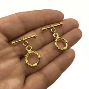 May include: Two gold-toned metal toggle clasps with a round, wire-wrapped loop. The clasps are designed for attaching to fabric or leather.