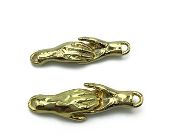 May include: Two gold-toned metal charms in the shape of hands holding each other. Each charm has a small loop at the top for attaching to a necklace or bracelet.