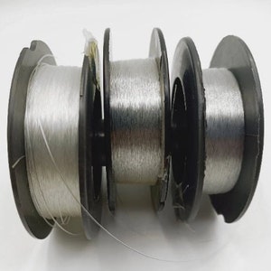 Puede incluir: Cuatro carretes de hilo de pesca plateado enrollados en carretes de plástico negro.