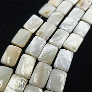 May include: A strand of white rectangular shell beads. The beads have a pearlescent sheen and are arranged in rows.