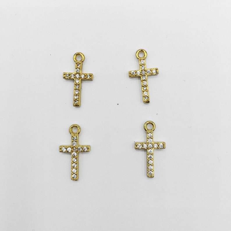 May include: Four gold-toned cross charms with clear rhinestone accents. Each cross charm has a loop at the top for attaching to jewelry.