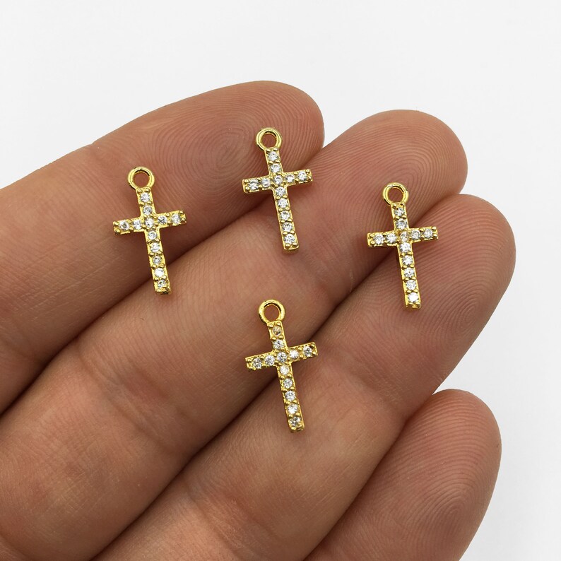 May include: Four gold-tone cross charms with clear crystal accents. Each charm has a loop at the top for attaching to a necklace or bracelet.