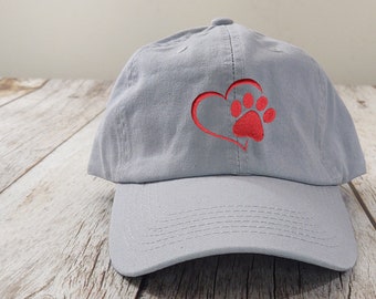 May include: A light gray baseball cap with a red embroidered heart and paw print design.