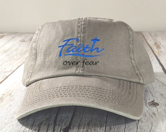 May include: A khaki baseball cap with the words "Faith over fear" embroidered in black and blue lettering.